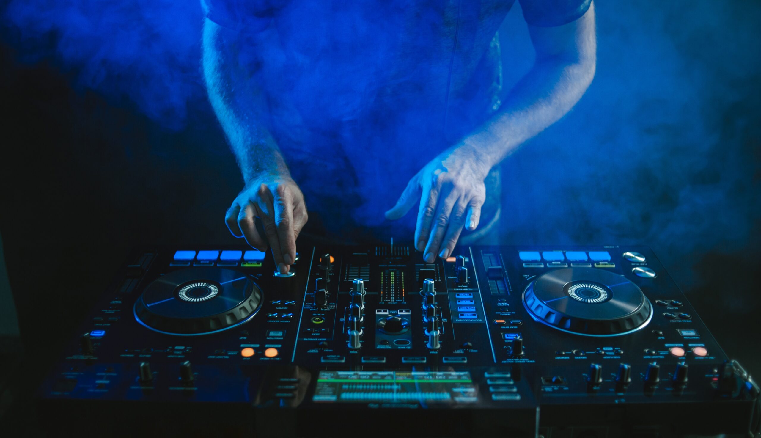 A closeup of a DJ working under the blue lights against a dark background in a studio